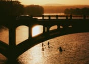 Thumbnail 6 of 12 - people swimming in a river under a bridge at sunset