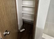 Thumbnail 17 of 18 - A white door with a silver handle is open to a small pantry with shelves.