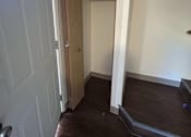 Thumbnail 9 of 18 - A white door is open to a hallway with a brown floor.