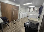 Thumbnail 19 of 27 - A laundry room with a washer and dryer, a black trash can, and a black chair.