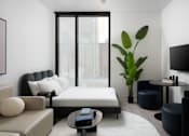 Thumbnail 12 of 24 - A living room with a large window, a sofa, a coffee table, and a potted plant at Miles at Ybor Apartments, Florida