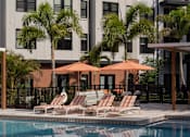 Thumbnail 6 of 19 - A pool area with chairs and umbrellas in front of a building.