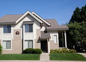 Thumbnail 15 of 33 - River Oaks at Rochester Hills Apartments: two-story beige townhome with manicured lawn and front walkway.