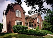 Thumbnail 13 of 33 - River Oaks at Rochester Hills Apartments brick townhome-style building with front steps and landscaped shrubs.