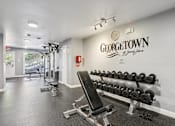 Thumbnail 22 of 33 - A gym with a row of dumbbells and a bench in front of a wall with the word "Georgetown" on it.