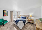 Thumbnail 11 of 43 - A bedroom with a large bed, a green chair, and a painting on the wall.