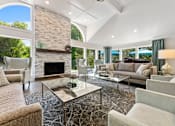 Thumbnail 21 of 33 - River Oaks at Rochester Hills Apartments clubhouse lounge with stone fireplace, sofas, glass coffee tables, and large arched