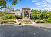 Thumbnail 18 of 33 - River Oaks at Rochester Hills Apartments clubhouse entrance with stone steps, railings, and landscaped flower beds.