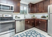 Thumbnail 2 of 33 - Kitchen with stainless appliances, dark wood cabinets, white backsplash, patterned rug at River Oaks in Rochester Hills.