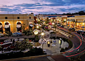 Thumbnail 33 of 33 - Dusk view of lit plaza and storefronts near River Oaks at Rochester Hills Apartments.
