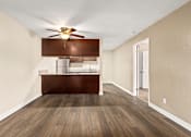 Thumbnail 20 of 36 - A room with a ceiling fan and a wooden floor leading to a kitchen area.
