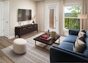 Thumbnail 9 of 29 - A living room with a dark blue sofa, a wooden coffee table, a white ottoman, and a flat-screen TV mounted on the wall.
