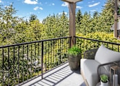 Thumbnail 8 of 29 - A balcony with a metal railing, a grey couch, and a potted plant.