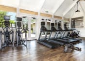 Thumbnail 21 of 25 - Three Bedroom Apartments in Santa Cruz CA - Cypress Point - Gym with Black Treadmill and Elliptical Machines with Screens, Wood Floors, and Windows Under a Vaulted Ceiling with Lighting and Fan