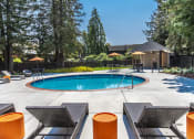 Thumbnail 15 of 25 - Circular pool surrounded by deck chairs, orange tables, trees and grass.