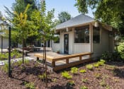 Thumbnail 25 of 25 - Trees and flowers leading up to lounge building and patio with wooden benches as outdoor seating attached to lounge.