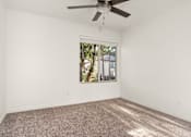 Thumbnail 21 of 33 - A room with a ceiling fan and a window showing trees and a building outside.