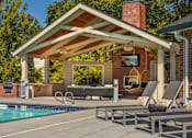 Thumbnail 27 of 29 - A poolside patio with a covered seating area and a brick chimney.