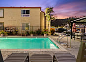 Thumbnail 3 of 33 - A pool surrounded by lounge chairs and a building in the background.