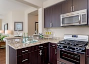 Thumbnail 5 of 29 - A kitchen with brown cabinets and a granite countertop.