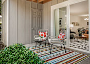 Thumbnail 11 of 48 - Covered patio seating area with colorful striped rug at Canyon Creek Apartments, Wilsonville, OR