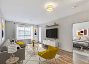 Thumbnail 7 of 28 - A living room with a grey couch, yellow chair, and a television.