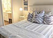 Thumbnail 6 of 20 - A bed with a white headboard and striped comforter with a white lamp on the bedside table.