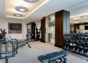 Thumbnail 39 of 48 - a gym with weights machines and a television on the wall at VORA LUX, San Diego, CA 92120