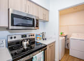 Thumbnail 17 of 44 - A small kitchen with a stove, microwave, and washing machine.