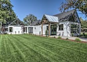 Thumbnail 20 of 29 - A white house with a black roof and a green lawn in front.