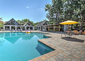 Thumbnail 12 of 27 - A large outdoor swimming pool with a yellow umbrella and a house in the background.