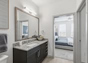 Thumbnail 23 of 55 - A bathroom with a sink, mirror, and a bedroom in the background.