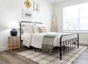 Thumbnail 6 of 15 - A bedroom with a bed, a lamp, a surfboard, and pictures on the wall.