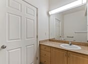 Thumbnail 25 of 36 - A bathroom with a white door, a sink, and a mirror.
