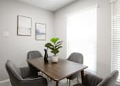 Thumbnail 9 of 18 - A table with chairs and a potted plant in a room with white walls.