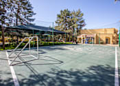 Thumbnail 16 of 18 - A tennis court with a green fence and a building in the background.
