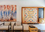 Thumbnail 29 of 48 - A game of Scrabble is set up on a wall next to a painting of trees.