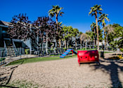 Thumbnail 37 of 44 - A playground with a red slide and a blue slide in the middle of a sandy area.