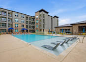 Thumbnail 42 of 55 - A large swimming pool in front of a building with a sun lounger.