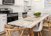 Thumbnail 6 of 12 - A modern kitchen with a wooden table and white chairs.