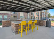 Thumbnail 36 of 38 - a patio with a bar with yellow chairs and a grill