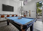 Thumbnail 13 of 30 - A pool table with a blue cloth and a television mounted on the wall.