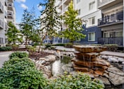 Thumbnail 26 of 30 - A waterfall in a garden in front of apartment buildings.