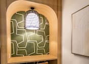 Thumbnail 57 of 57 - A wooden desk with a lamp and a chair in front of a geometric patterned wall.