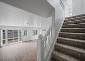 Thumbnail 32 of 55 - A staircase with a carpeted runner and white balusters leads to a brightly lit room with white walls and a wooden floor at Hillsdale Garden Apartments, San Mateo, CA 94403