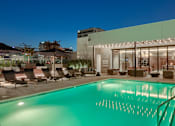 Thumbnail 23 of 24 - A pool in front of a building with lights on.