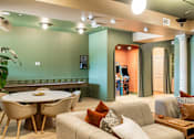 Thumbnail 23 of 41 - A living room with a white table and chairs, a grey couch, and a green wall.