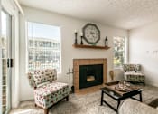 Thumbnail 14 of 21 - A living room with a fireplace, two chairs, and a clock on the wall.
