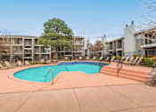Thumbnail 1 of 21 - A swimming pool surrounded by lounge chairs and trees in a residential area.
