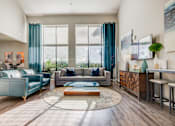 Thumbnail 13 of 27 - A living room with a grey couch, a blue couch, a coffee table, and a painting on the wall.